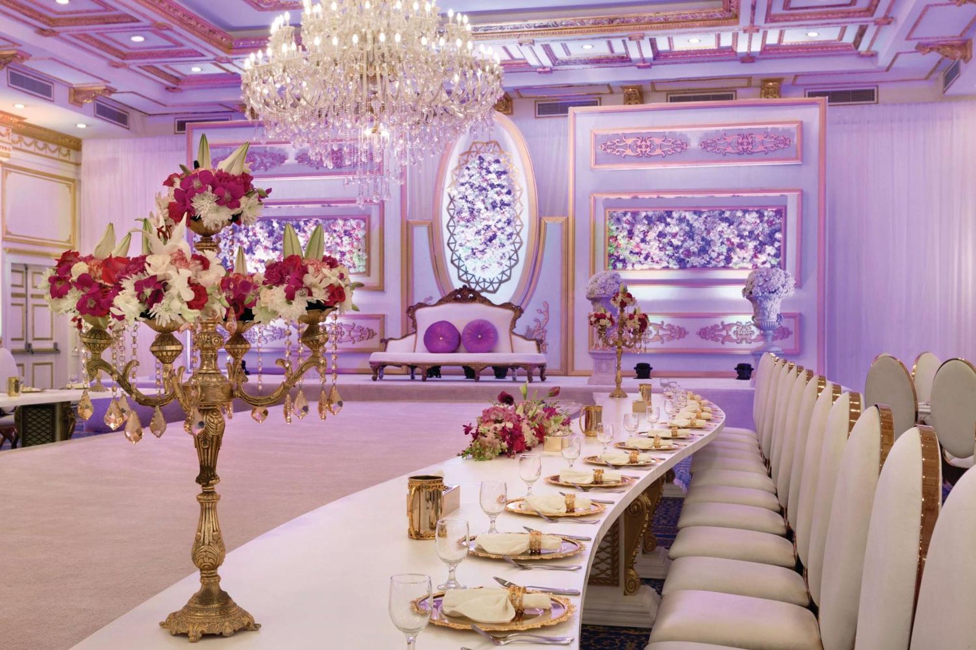 Grand Regency Doha, Trademark Collection By Wyndham Dış mekan fotoğraf The photo displays an elegantly decorated banquet or dining hall. It features a long, curved table set for a formal event, with fine china and floral centerpieces. Luxurious decorations include a grand chandelier hanging from the ceiling, and the wal