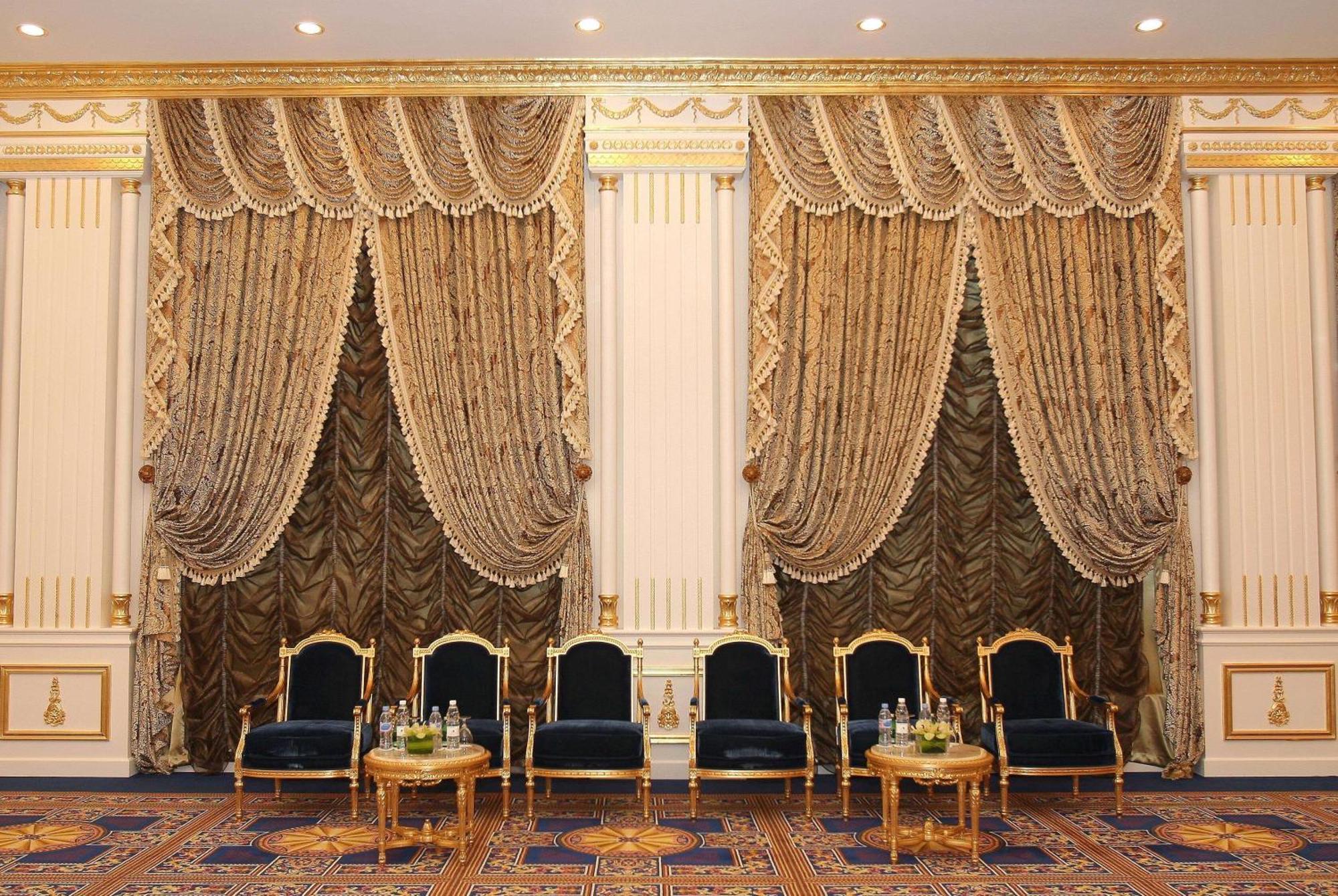 Grand Regency Doha, Trademark Collection By Wyndham Dış mekan fotoğraf The photo shows an elegantly decorated interior space. There are two sets of opulent curtains on the walls, featuring rich fabrics with ornate designs and gold accents. The curtains are paired with decorative tiebacks. In front of the curtains, there