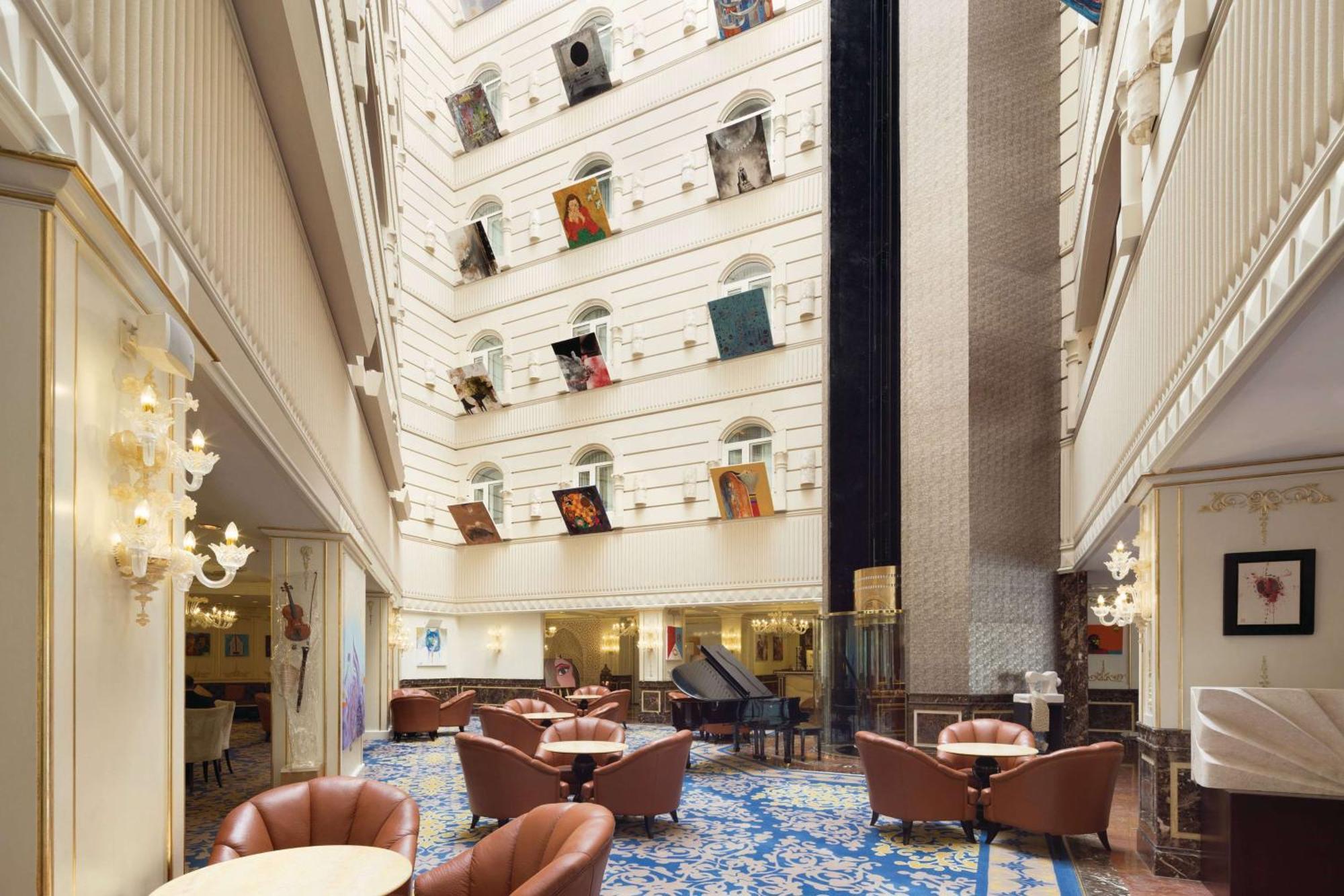 Grand Regency Doha, Trademark Collection By Wyndham Dış mekan fotoğraf The photo depicts the interior of a spacious, upscale hotel lobby. The design features high ceilings and multiple levels, with large windows that create a bright and airy atmosphere. Elegant light fixtures adorn the walls, and the floor is covered wi