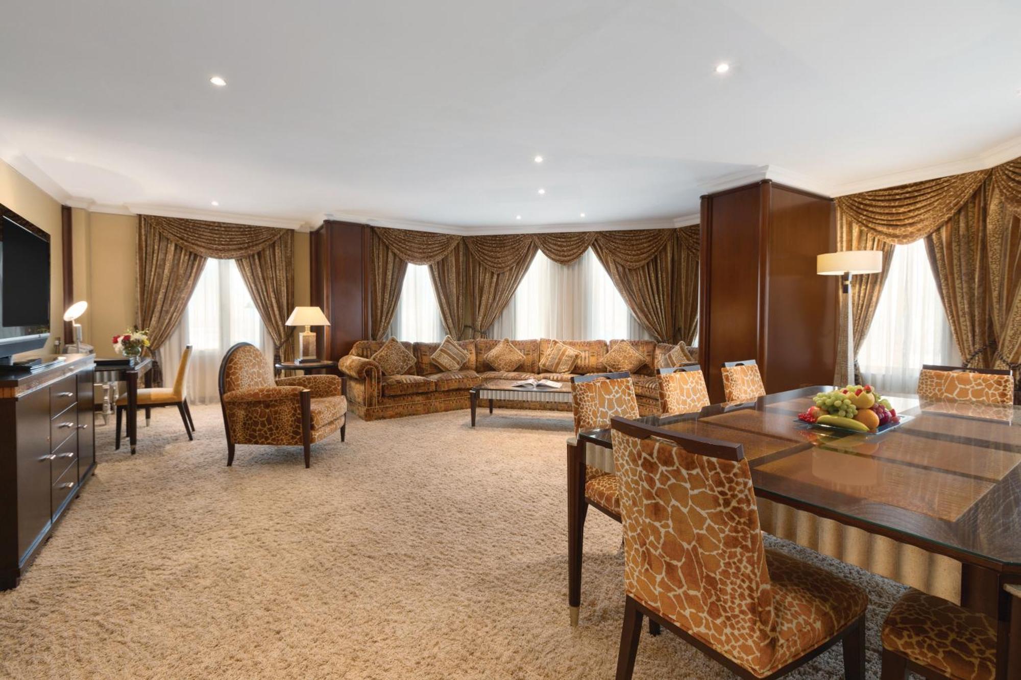 Grand Regency Doha, Trademark Collection By Wyndham Dış mekan fotoğraf The photo shows a spacious and elegantly designed living area. There are large windows dressed with luxurious curtains, allowing natural light to fill the room. The seating arrangement features a comfortable sofa with various cushions and several sty