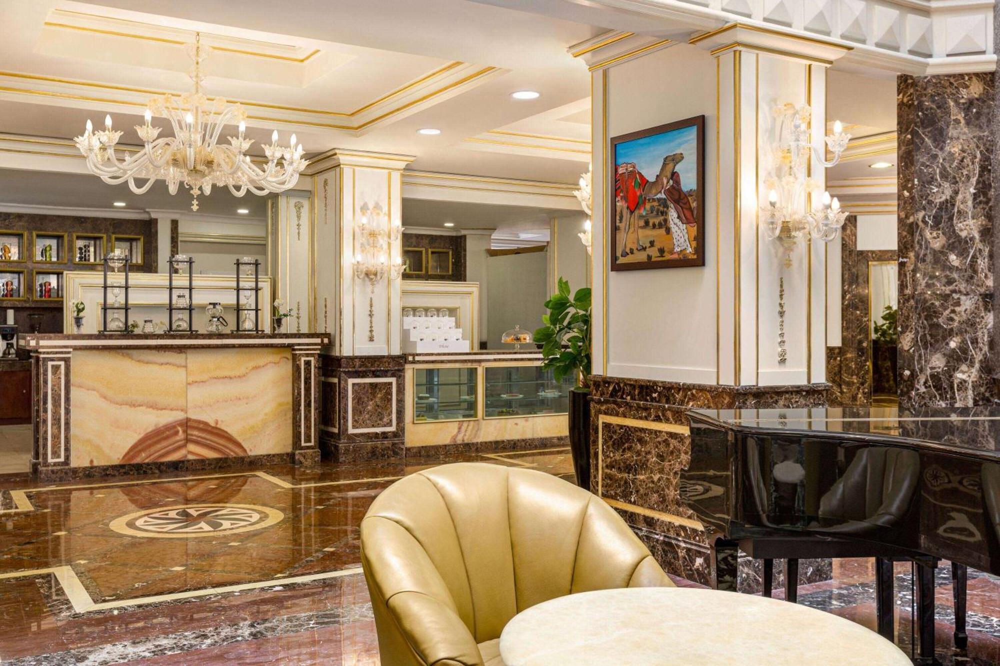 Grand Regency Doha, Trademark Collection By Wyndham Dış mekan fotoğraf The photo depicts an elegant hotel lobby interior. It features a polished marble floor with intricate patterns. In the background, there is a reception desk made of marble and wood, with decorative elements and a glass display. On the walls, you can 