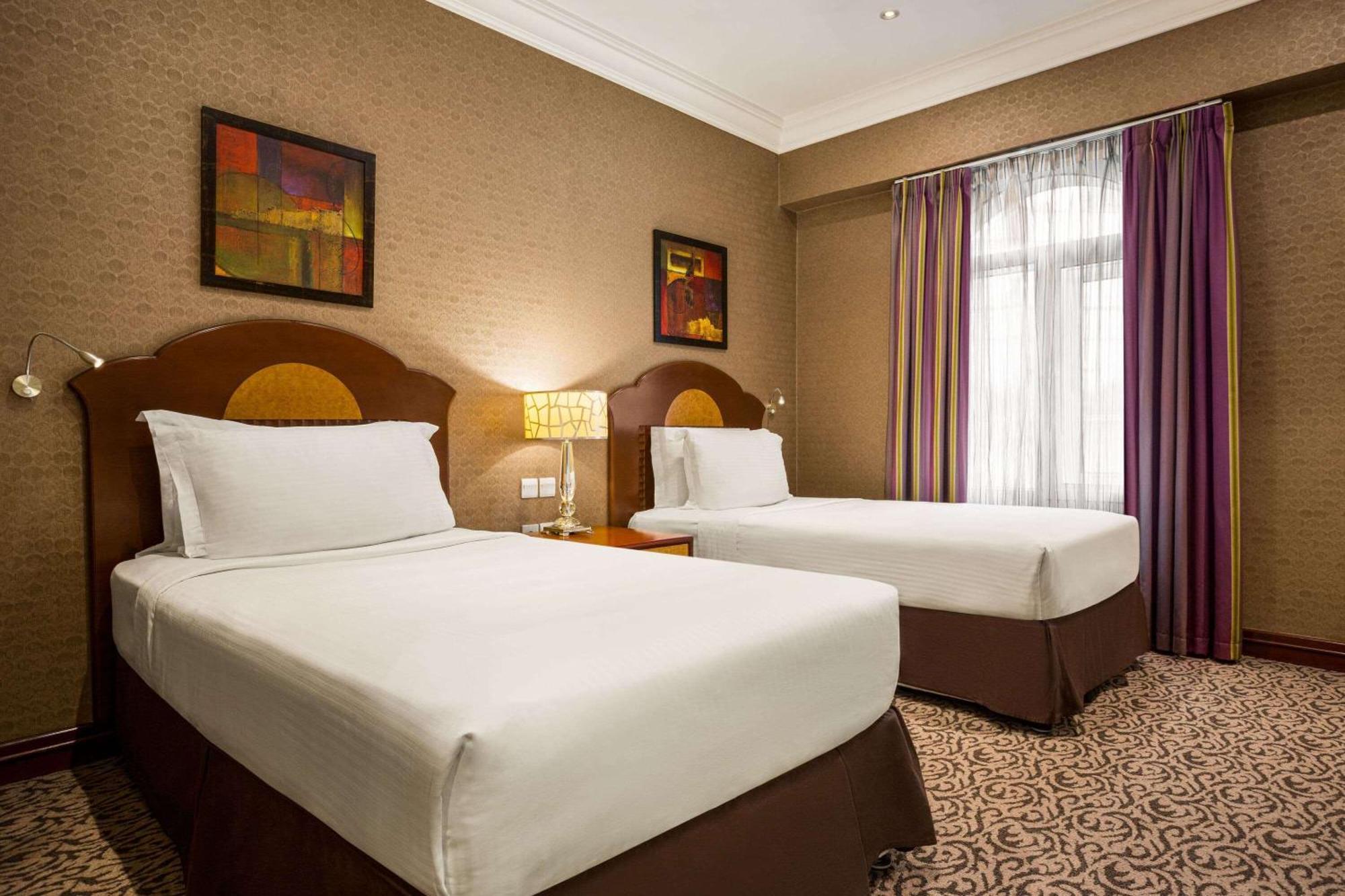 Grand Regency Doha, Trademark Collection By Wyndham Dış mekan fotoğraf The photo shows a hotel room featuring two single beds with white bedding and dark brown upholstered headboards. There is a bedside table with a lamp between the beds. On the walls are two abstract paintings, and large windows dressed with sheer curt