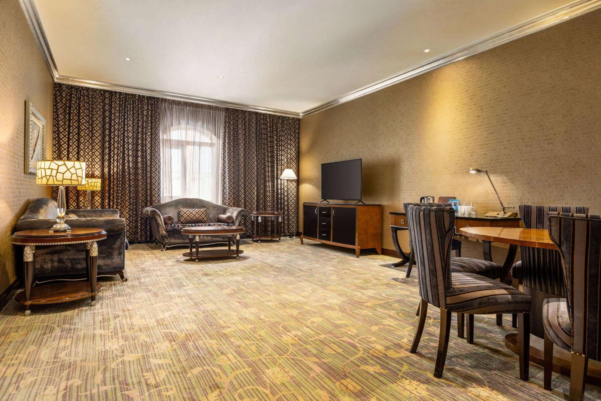 Grand Regency Doha, Trademark Collection By Wyndham Dış mekan fotoğraf The photo shows a spacious lounge or living area. It features a comfortable seating arrangement with a dark-colored sofa and armchairs, arranged around a coffee table. There's a dining table with matching chairs, suggesting it can accommodate meals o